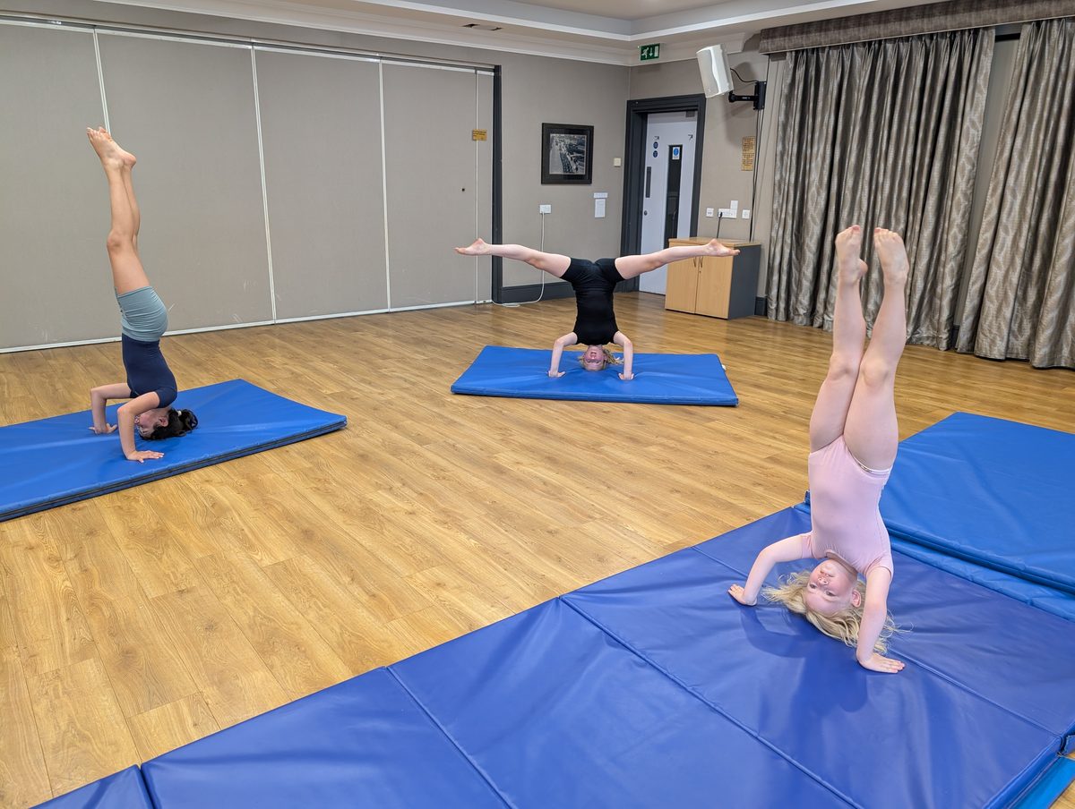 Three dancers holding headstands on mats