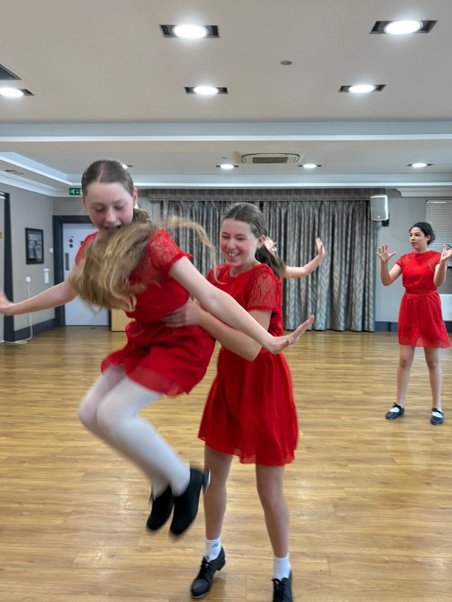 Two dancers in red mid-jump in a tap class