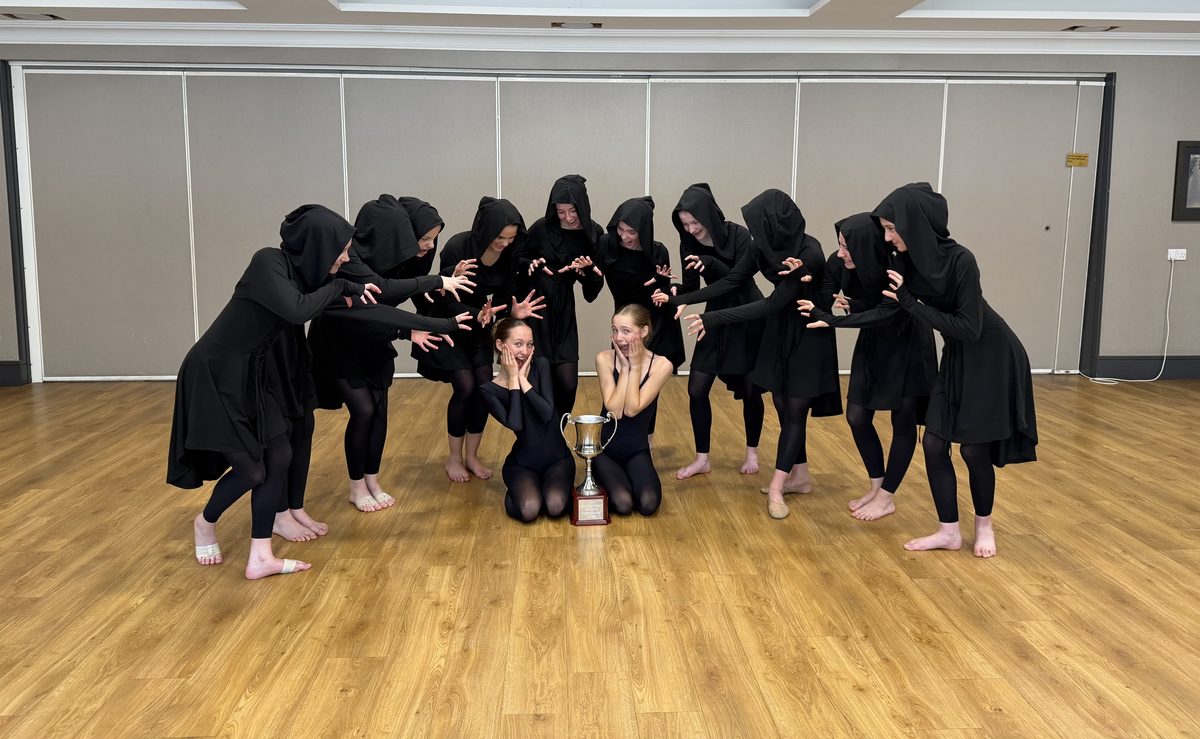 The Senior competition group in black hooded costumes with a trophy